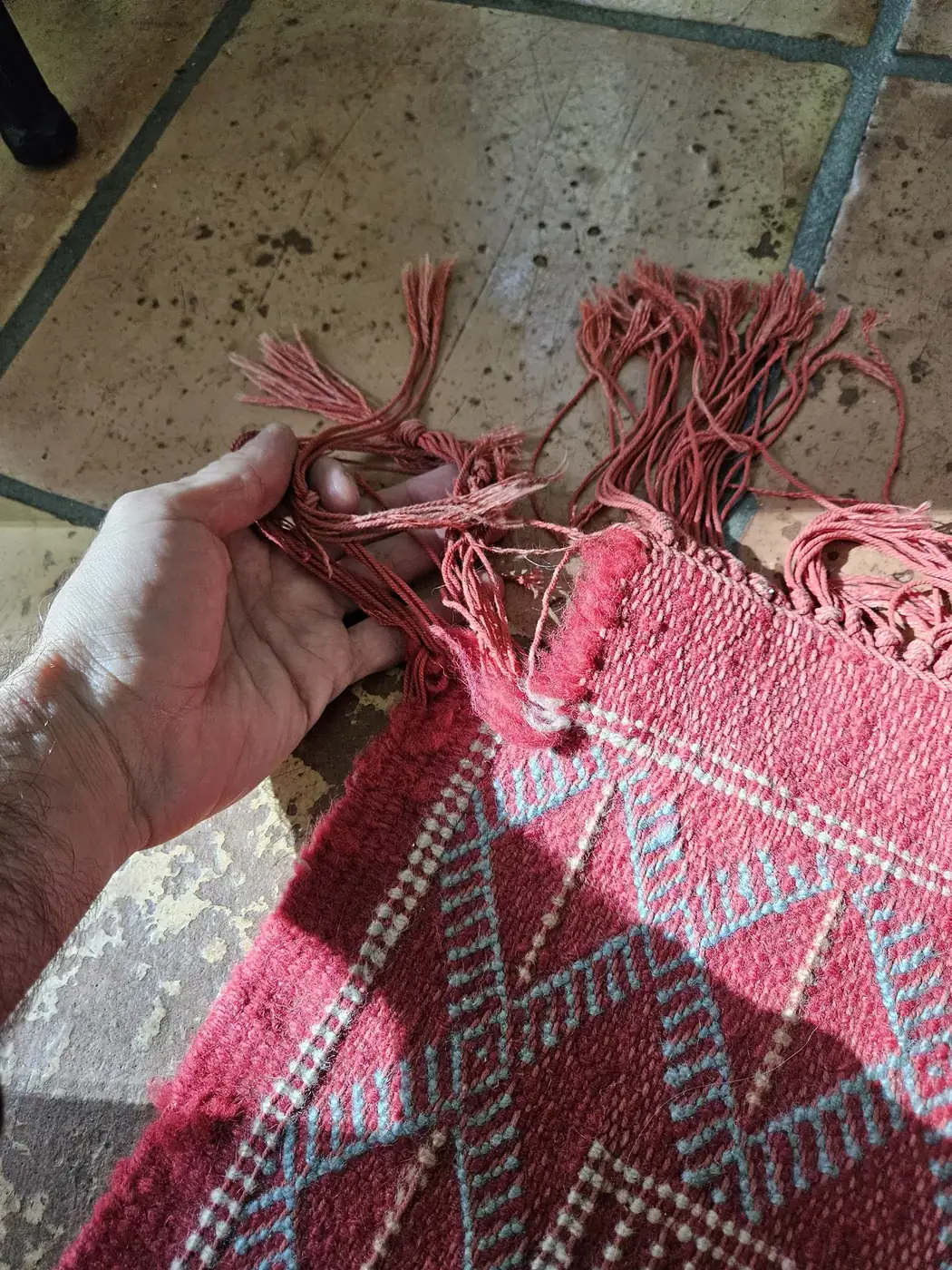 Hands holding the worn pink fringe of a rug before repair