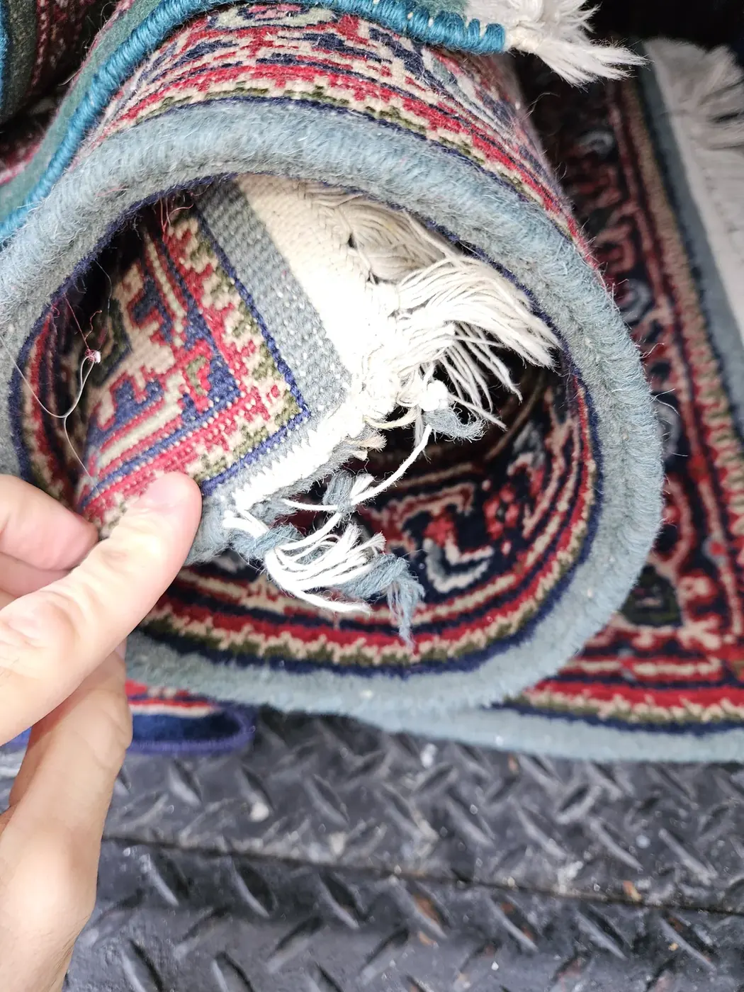 Rolled red rug with its fringe repaired by hand