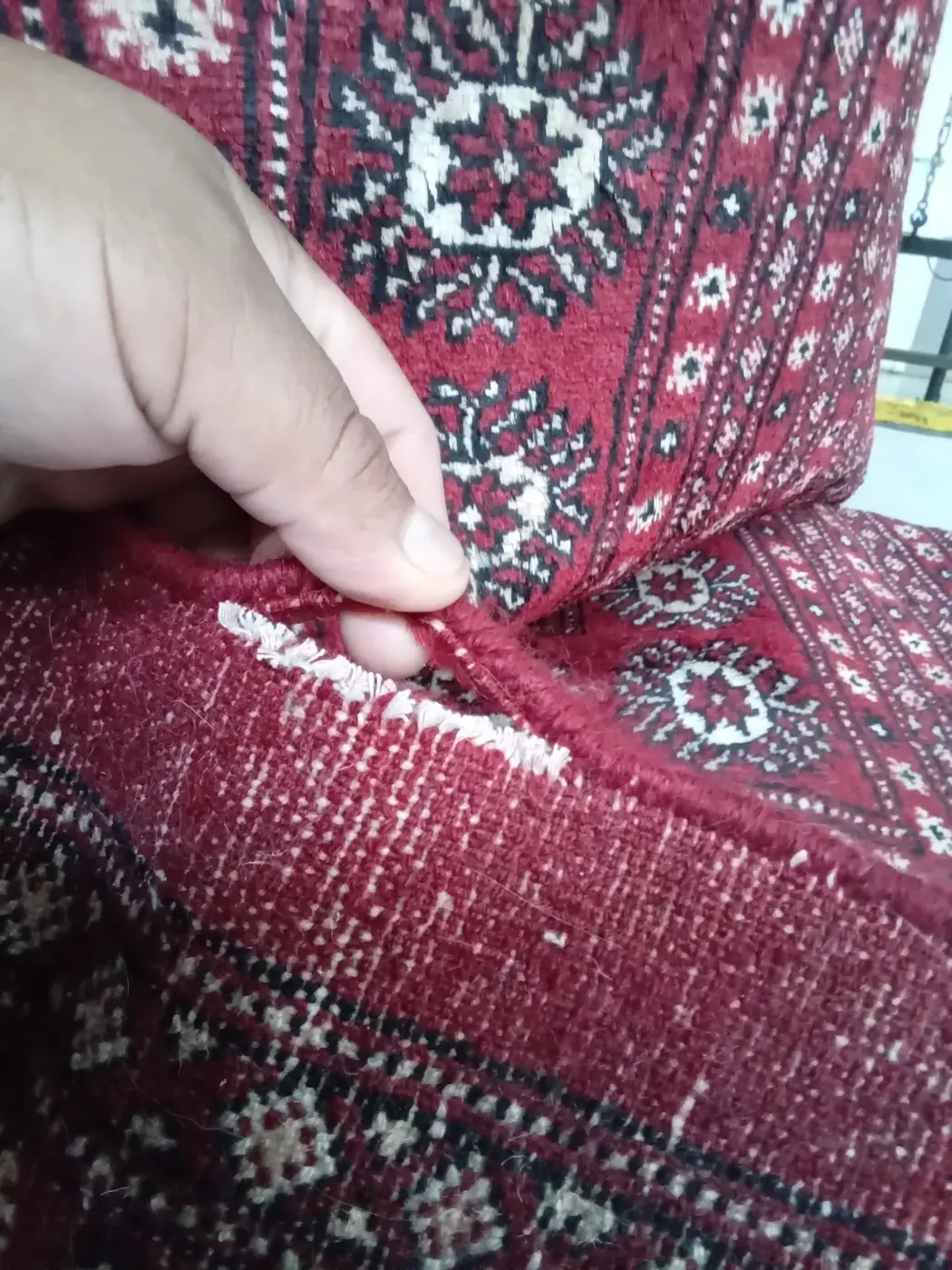 Hands examining a tear in a red Bokhara rug at the repair bench